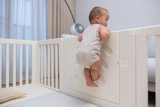 Curious baby trying to climb playpen fence