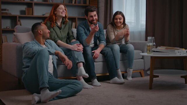 Four multiracial friends watching television tv laughing smiling carefree at home party discuss comedy funny movie cinema film multiethnic people watch modern smart tv humorous show women men together