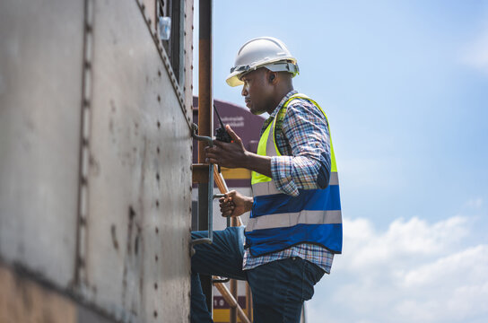 Railway Engineer Using a Walkie-Talkie on a Train, African American Man in Hard Hat and Safety Vest Working, Railroad Worker Climbing onto a Freight Car