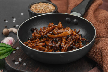 Fried Shimeji mushrooms with garlic, basil, and spices in a pan, served on a dark background