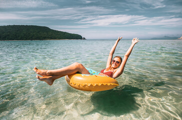 Smiling woman floating in clear sea on donut-shaped inflatable. Carefree summer vibes, sunshine, and joy perfect vacation moment.