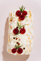 Elegant raspberry meringue roll cake on pink background with festive decoration