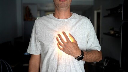 A man in a white t-shirt places his hand on his chest with a glowing light effect under his hand, symbolizing heart, energy, or inner power.