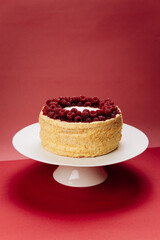 Homemade raspberry cake on a white stand against red background, close up food shot