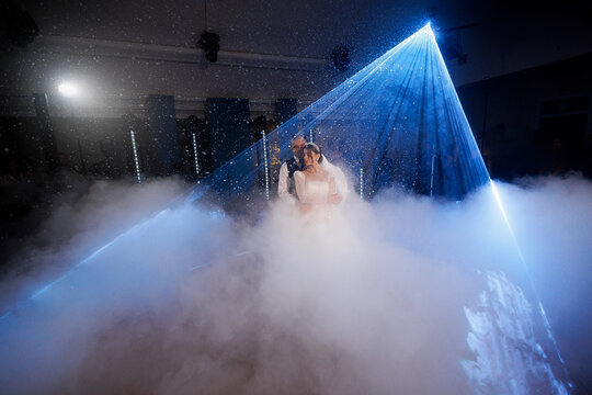 Couple dances together under a dramatic light show at a wedding reception