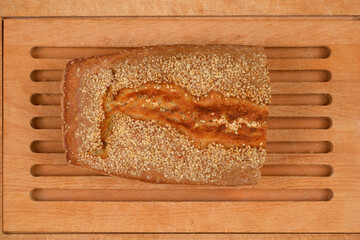 An overhead shot of a fresh loaf of bread covered in sesame seeds resting on a wooden cutting board
