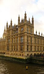 View of the Palace of Westminster in London, captured from across the Thames River. Detailed Gothic architecture, spires, and numerous windows of building. British politics, history, and travel.
