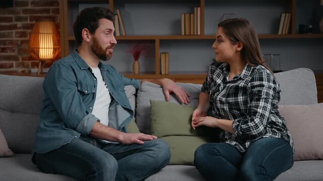 Caucasian couple talking at home emotional husband sharing amazing news with wife two people multiracial girlfriend boyfriend talk man Hispanic woman on couch in living room communicating in evening