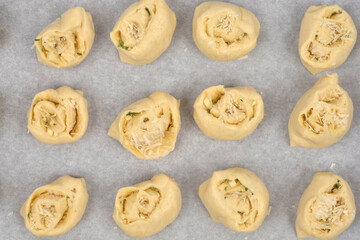 An overhead view shows unbaked rolls filled with garlic and parmesan, arranged in rows on a baking sheet lined with parchment paper