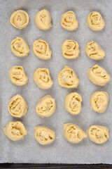 An overhead view shows unbaked rolls filled with garlic and parmesan, arranged in rows on a baking sheet lined with parchment paper