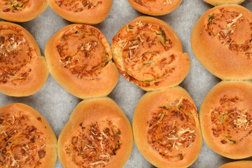 An overhead shot shows several golden-brown baked rolls topped with melted cheese and herbs, arranged on a baking sheet