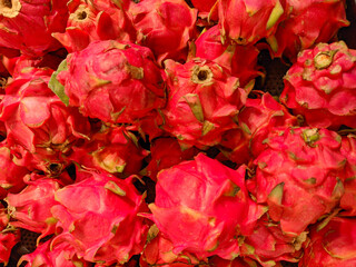A large pile of fresh, red dragon fruit. The unique, scaly skin and bright color of the tropical fruit create an organic and appealing texture, perfect for food-themed visuals.