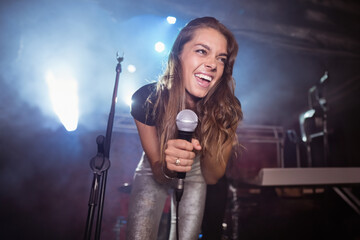 Stage lights are glowing through fog around handheld microphone next to keyboard on concert stage