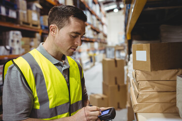 Scanning man using handheld barcode scanner in warehouse aisle, with cardboard boxes, copy space
