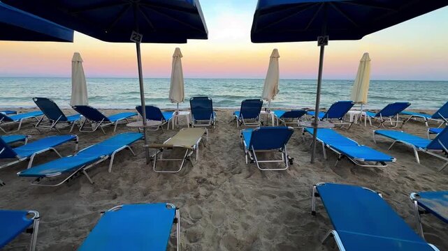 Blue sunbeds on a Paralia beach at sunset over the Aegean Sea