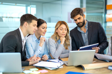 Dedicated business people in a meeting discussing strategy while reviewing data from laptop and reports