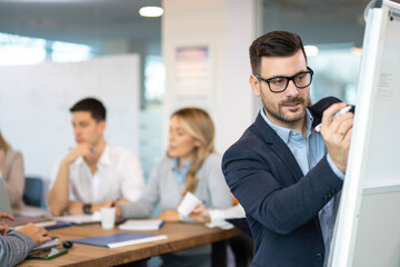 Businessman drawing charts on whiteboard during presentation in front of colleagues