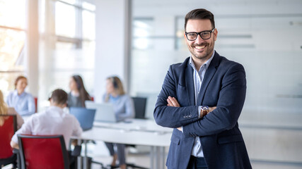 Businessman standing with crossed arms in office with colleagues in background
