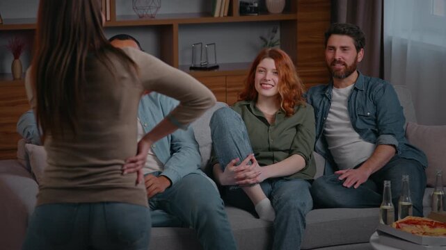 Four happy friends at home party playing pantomime game multiracial men women buddies guess woman showing forms funny play having fun diverse people guessing asking questions laughing talking smiling