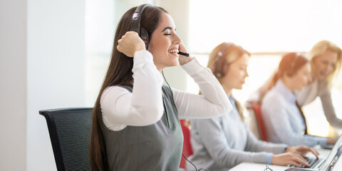 Woman with headset working alongside female colleagues in call center at laptops