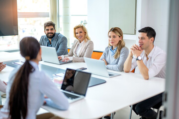 Business people sitting with laptops around conference table in meeting room