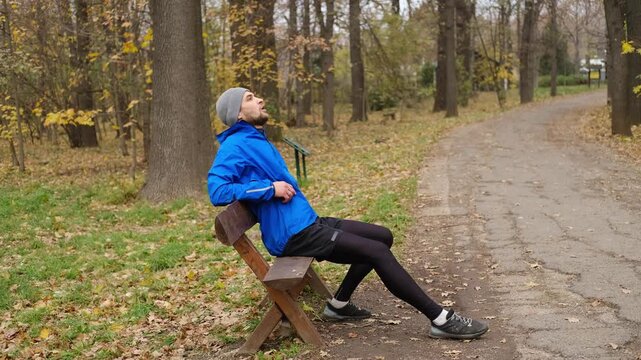 Man in blue sports jacket exercising on parallel bars in autumn park, training arms and upper body strength. 4K horizontal footage.