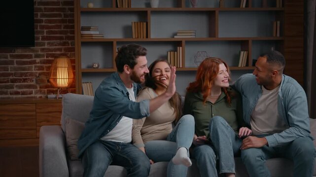 Multiethnic four friends jumping running falling on couch at home party giving high five laughing smiling diversity group of best buddies gathering together men women on sofa having fun fooling unity