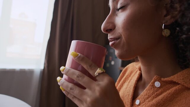 Closeup of young Biracial woman savoring first sip of her hot morning coffee, capturing cozy and refreshing start of day
