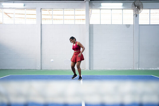 Female pickleball player serving ball on indoor court