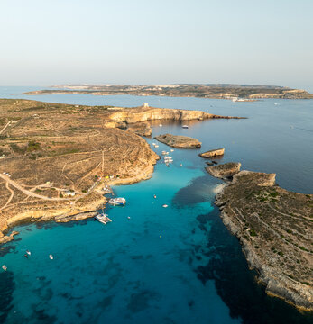 Aerial view of the azure waters embracing the rugged coastline and boats near Blue Lagoon, Comino, Malta.
