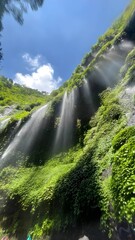 Sun rays beautifully illuminate a stunning cascade of water down a verdant jungle cliff, creating a serene and magical natural spectacle in paradise