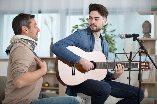 smiling teen son playing acoustic guitar for father at home