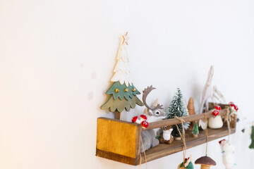 Stylish christmas decoration of children room. Christmas tree, reindeer, horse and mushroom cute toys on wooden shelf on wall. Modern minimalist decor of nursery for winter holidays