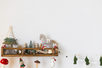 Stylish christmas decoration of children room. Christmas tree, reindeer, horse and mushroom cute toys on wooden shelf on wall. Modern scandinavian decor of nursery for winter holidays