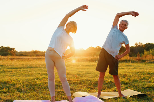 Elderly couple practicing yoga outdoors during sunset in a peaceful park setting