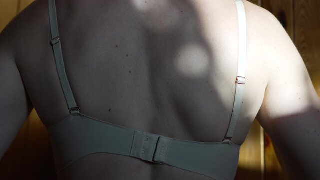 Bra unhooking woman's back indoors in sunlight for privacy and routine.