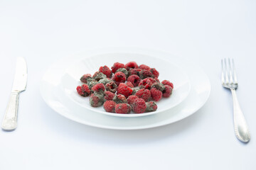 A serving plate with raspberries visibly spoiled by mold, symbolizing food waste and decay.