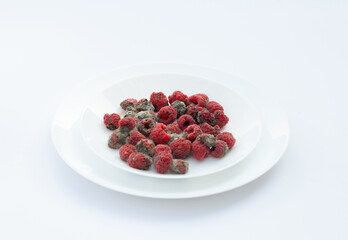 White plate full of raspberries infected by mold and fungus, representing food spoilage.