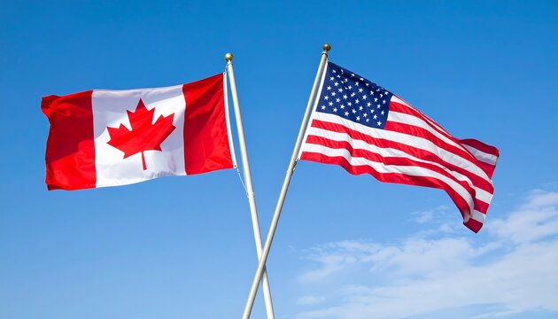 Two national flags, the Canadian and American flags, wave against a clear, light blue sky.