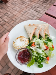 Waiter serving grilled goat camembert cheese with cranberry sauce, salad, and toast
