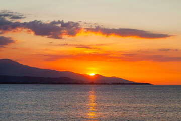 Obraz premium A stunning golden sunset over the sea, viewed from Cristo Rei Beach, the Dili coastline in Timor-Leste. The sun descends behind a mountain silhouette, creating a tranquil and peaceful atmosphere