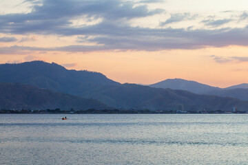 A tranquil dusk view in Dili, Timor-Leste. The silhouette of layered mountains creates a sense of depth over the peaceful sea, under a sky with a soft pastel color palette
