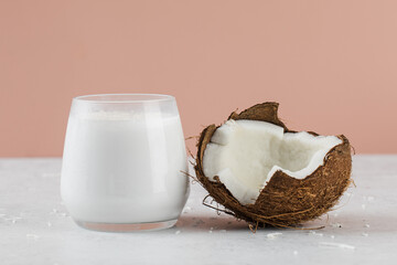 Fresh coconut milk in glass with whole and halved coconuts on pink background. 