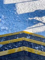 Close-up view of icy wooden steps with yellow safety strips leading into a snowy path