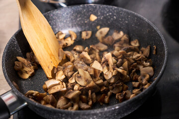 Mushrooms being in a skillet with a wooden spatula during dinner preparation in a cozy kitchen