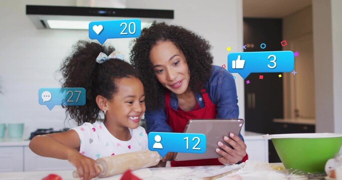 Following tablet recipe mother wearing apron and daughter rolling dough with rolling pin in kitchen