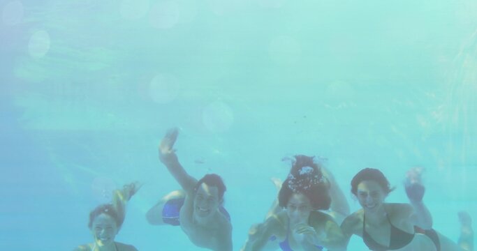 Smiling friends swimming underwater in pool, showing rising bubbles and rippling light patterns