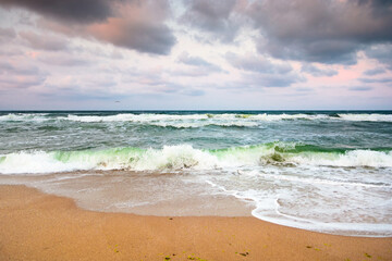 stormy beach scenery with waves splash on sand shore under scenic clouds on the sky. dark moody nature background for travel. scenic view of european coast