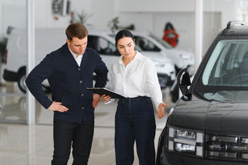 Friendly female car dealer standing at fancy car showroom and having consultations with a customer