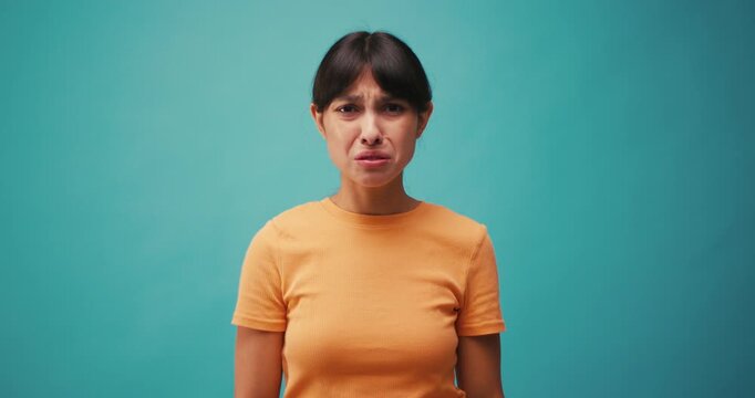 Hispanic woman feels disgust and holds nose on blue background
